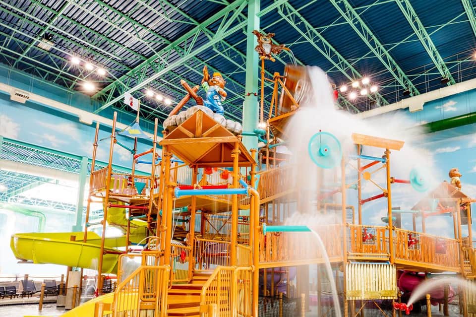 Indoor water park with colorful wooden play structure, water slides, and splash features