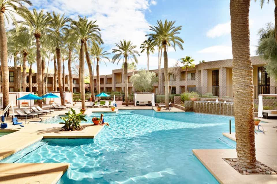 Resort pool surrounded by palm trees with lounge chairs and beige stone buildings