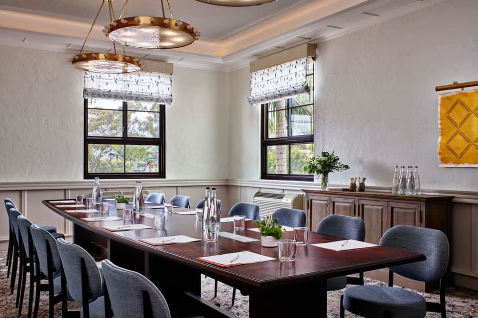 Professional conference room with long wooden table, gray chairs, brass chandeliers, and large windows