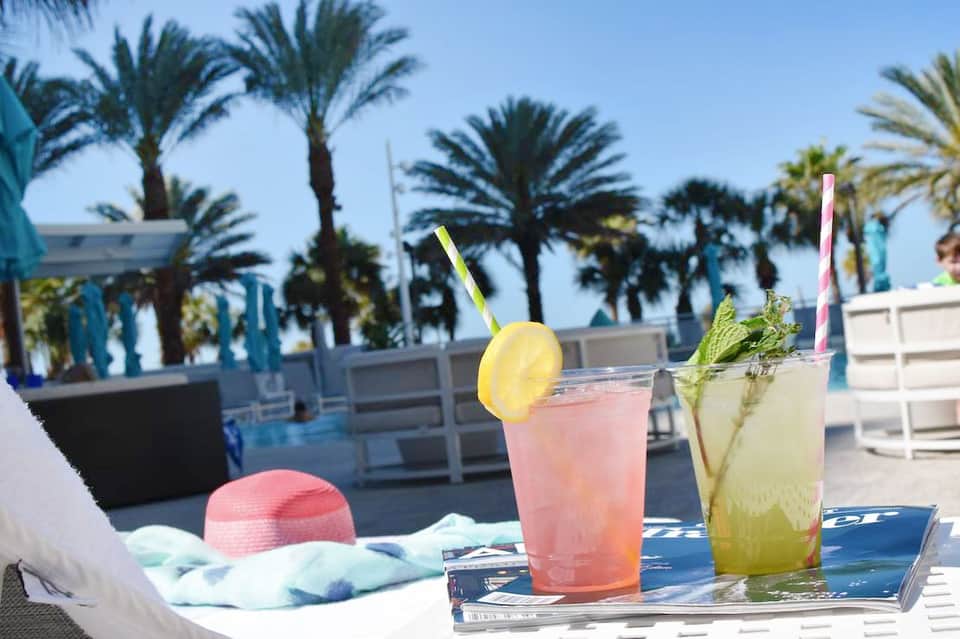 Tropical beachside cocktail bar with palm trees, pink and yellow drinks with garnishes on white lounge furniture