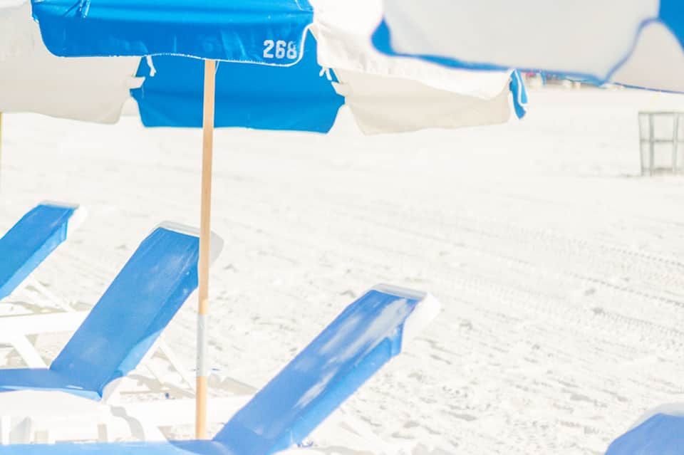 Blue and white beach umbrellas and lounge chairs on white sand beach