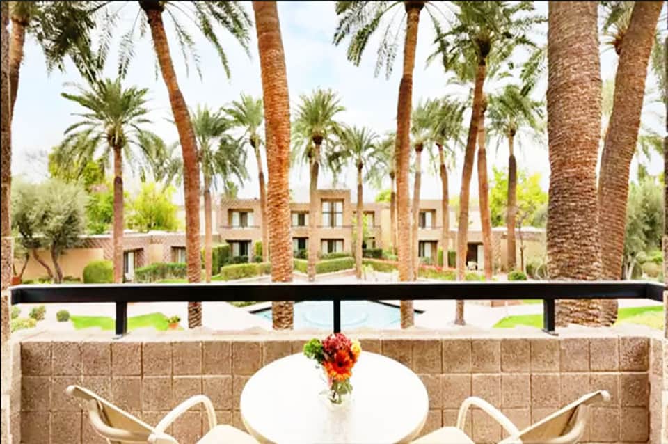 Balcony terrace with white chairs overlooking palm trees and resort courtyard with water feature