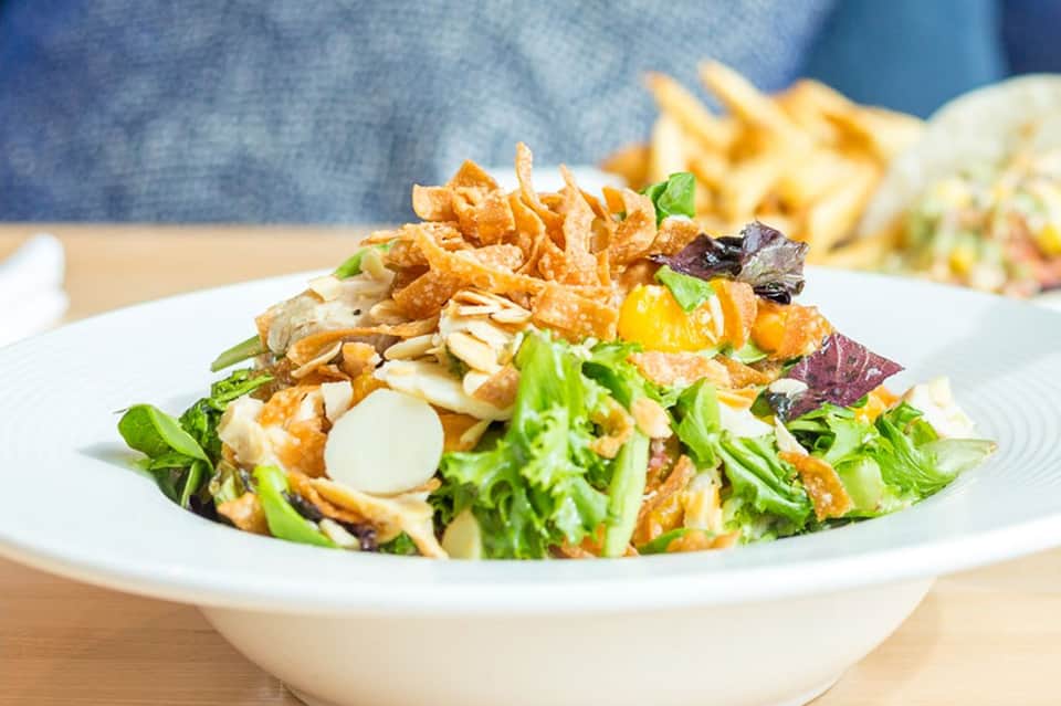Gourmet salad bowl with crispy noodles, greens, and garnishes on white plate