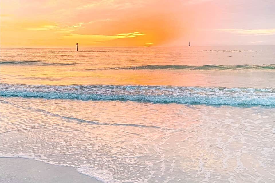 Golden sunset over calm ocean waves with blue water and sandy shore
