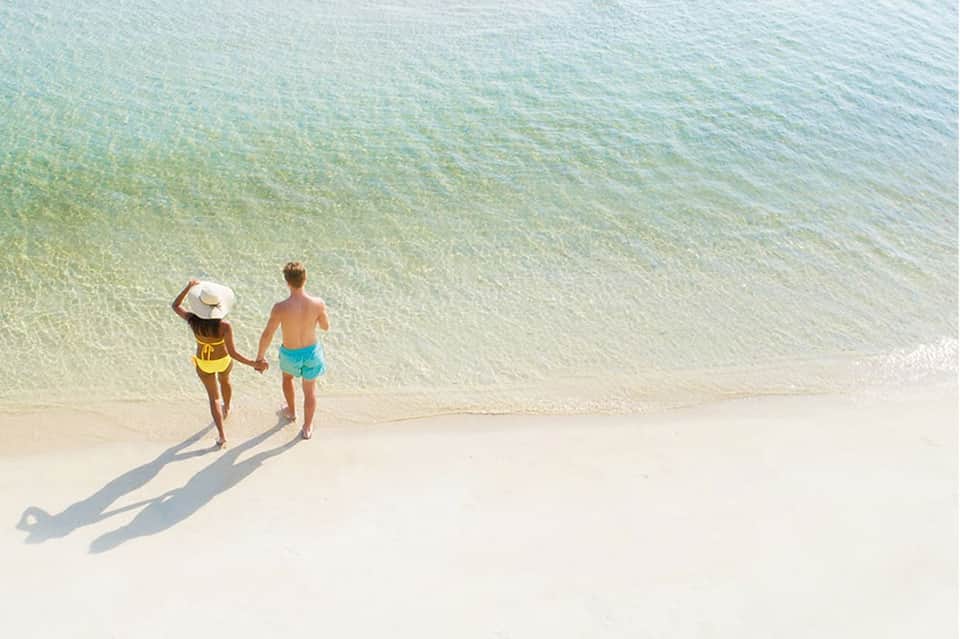 Aerial view of two children holding hands entering clear turquoise ocean water on a beach