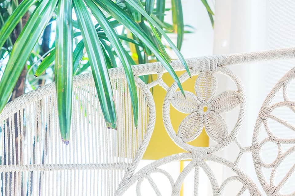 Close-up of green palm fronds over white patterned outdoor cushions and yellow accent pillow