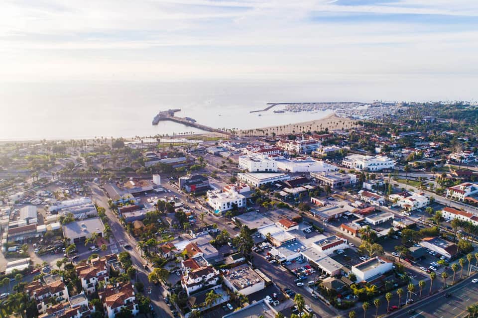 Aerial view of coastal resort town with ships, beach, palm trees, and residential buildings