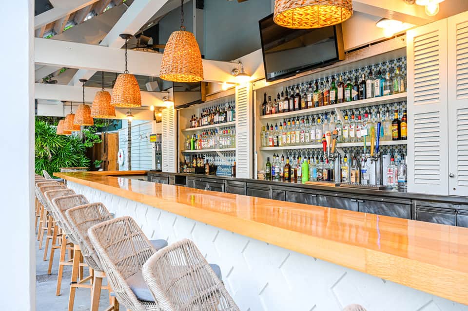 Modern bar interior with woven pendant lights, wooden counter, and fully stocked liquor shelves