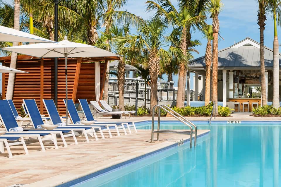 Resort pool with blue lounge chairs, white umbrellas, and palm trees surrounding the deck area