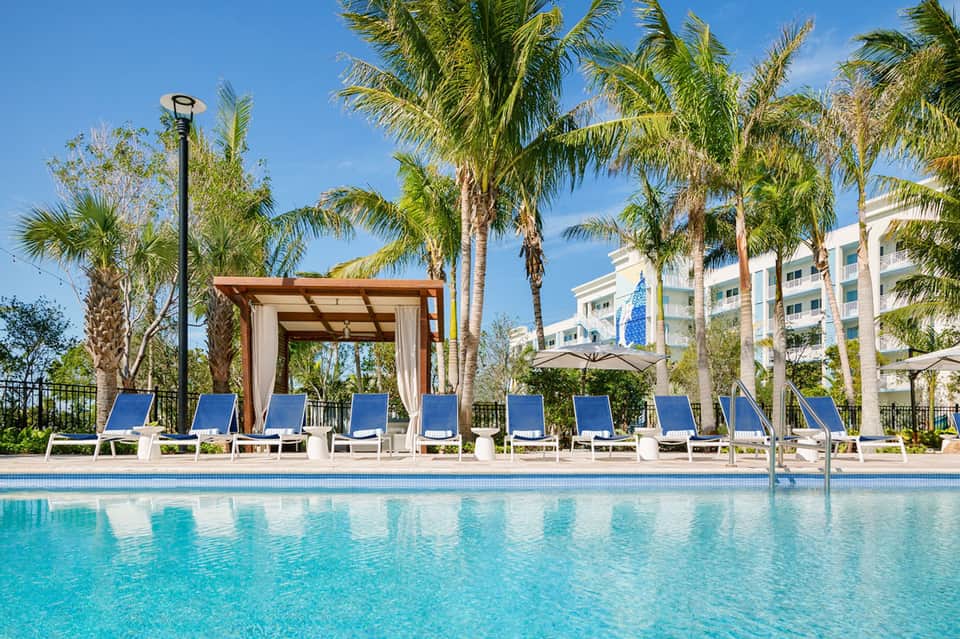 Luxury resort pool deck with palm trees, cabanas, and waterfront building