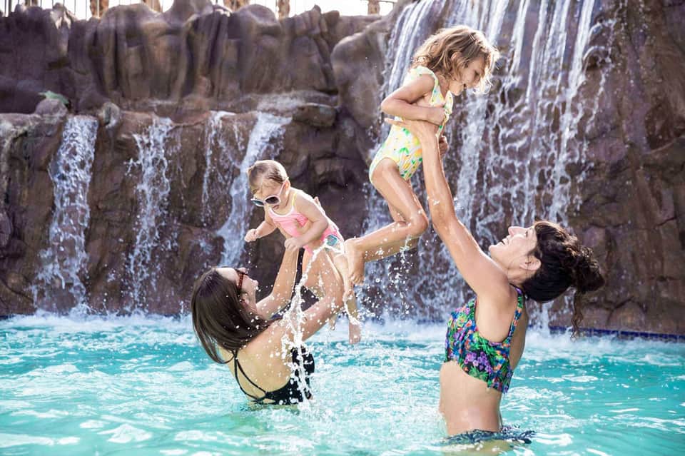 Adults and children swimming and playing in turquoise water with rocky waterfall formations