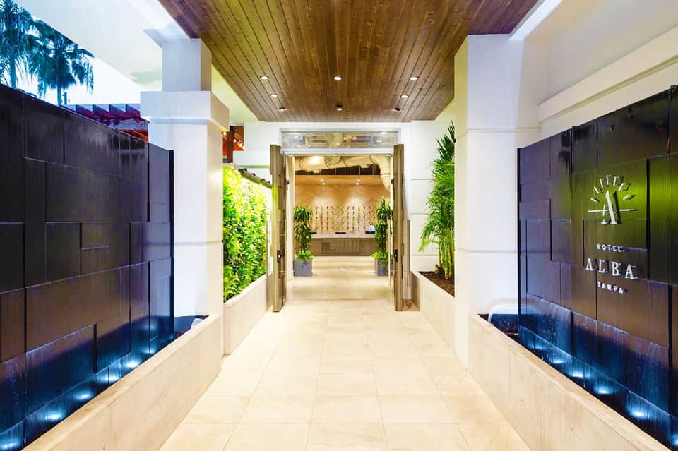 Modern hotel corridor with green living walls, wooden ceiling, and dark glass entrance doors leading to reception area