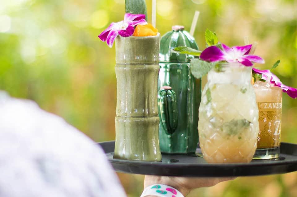 Tropical cocktails with colorful flowers on bamboo table overlooking garden landscape