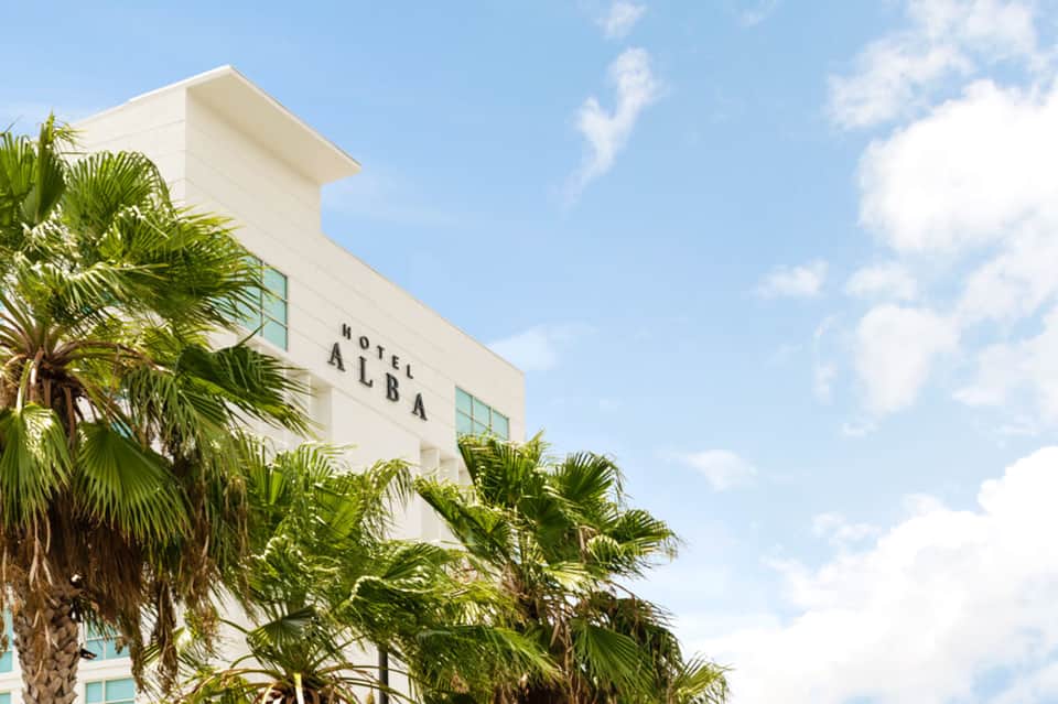 Modern white Hotel Alba building with palm trees against blue sky