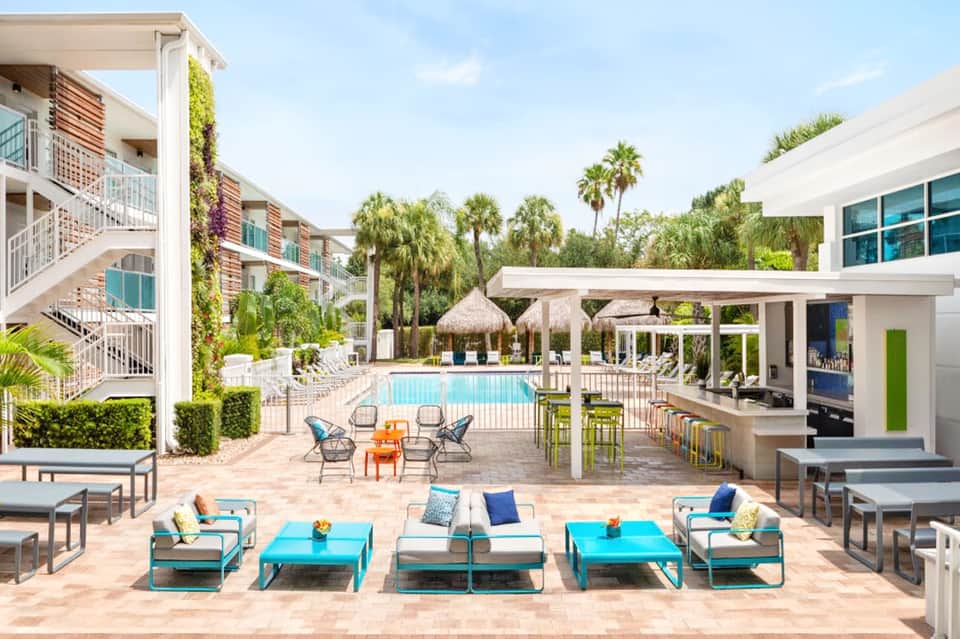 Resort courtyard with turquoise lounge chairs, pool, palm trees, and covered pavilions
