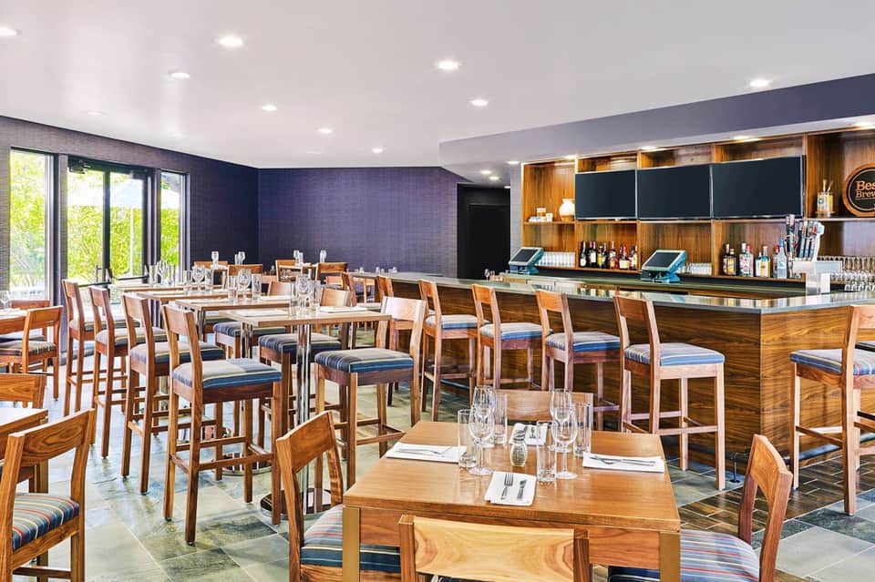 Modern restaurant interior with wooden bar, high-top seating, and blue accent wall