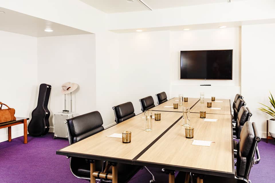 Modern conference room with long wooden table, black chairs, and wall-mounted TV
