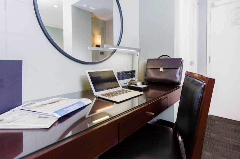 Modern hotel business center with desk, laptop, briefcase, round mirror, and professional furnishings
