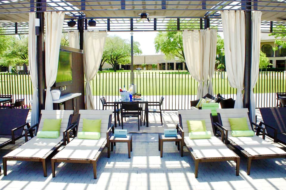 Outdoor pergola lounge area with sunbeds, green cushions, cream curtains, and manicured lawn views