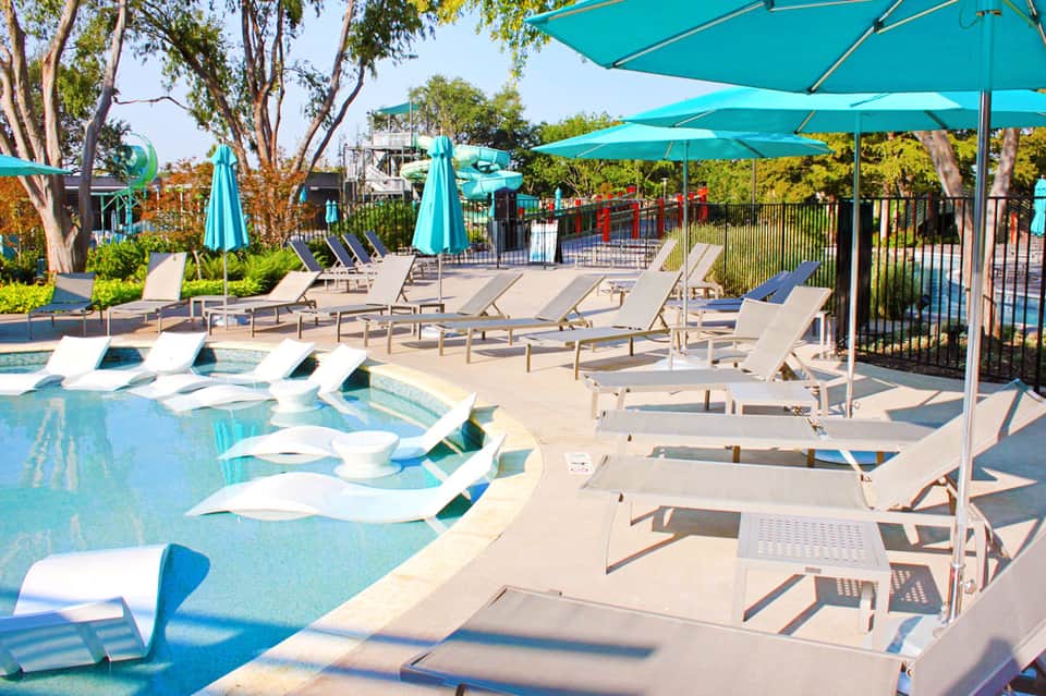 Resort pool deck with turquoise umbrellas, loungers, and shallow lounging pools under clear sky