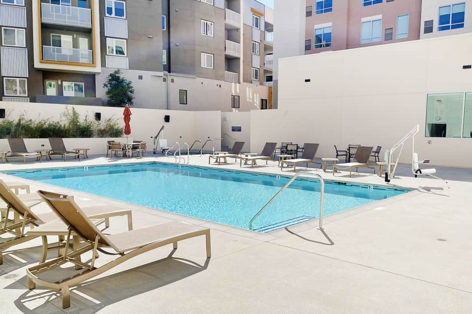 Resort swimming pool surrounded by lounge chairs and modern apartment buildings