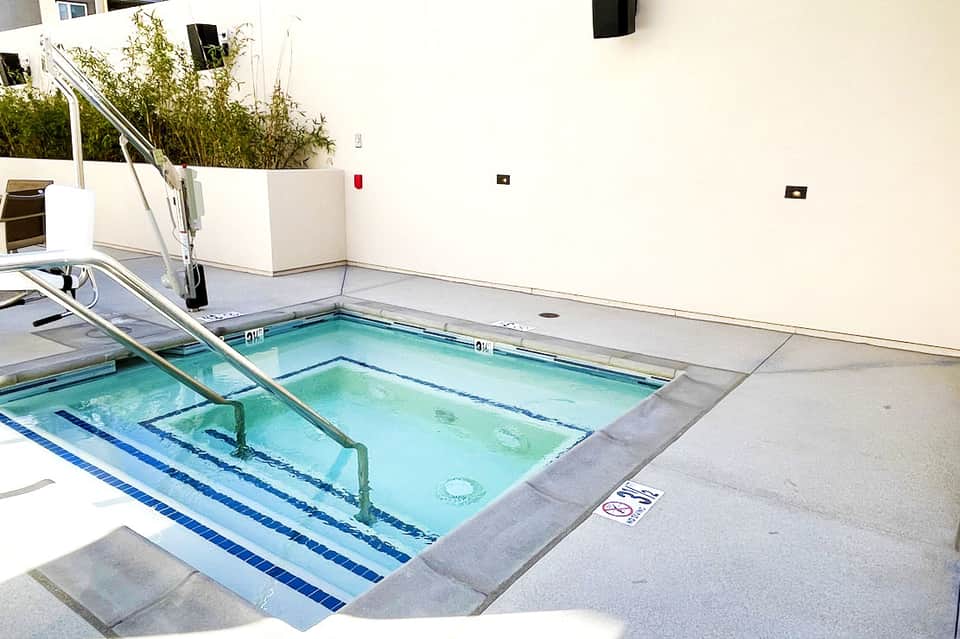 Outdoor lap pool with blue water and lane markers, surrounded by concrete deck and white building walls