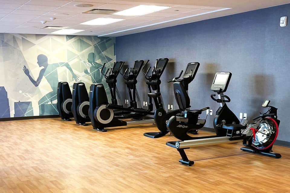 Indoor fitness center with stationary bikes, ellipticals, and exercise equipment lined against blue wall