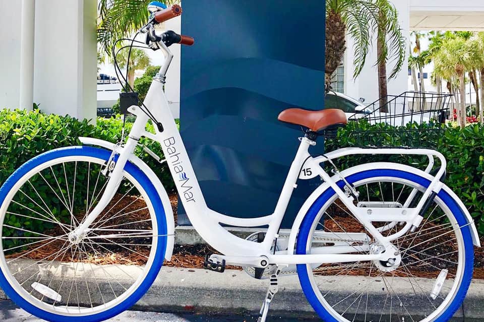 White and blue bike-share bicycle parked near tropical landscaping and modern buildings