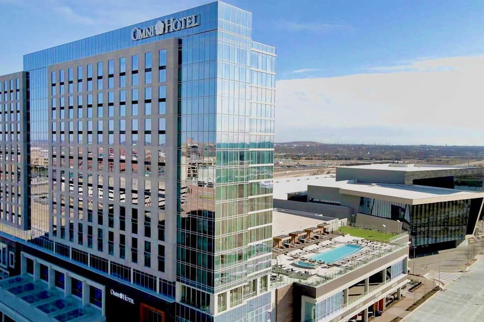 Modern Omni Hotel high-rise building with glass facade and rooftop pool overlooking cityscape and waterway.