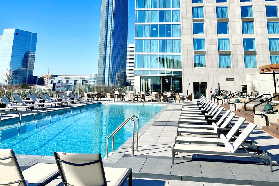 Modern hotel pool deck with loungers, high-rise buildings, and clear blue sky