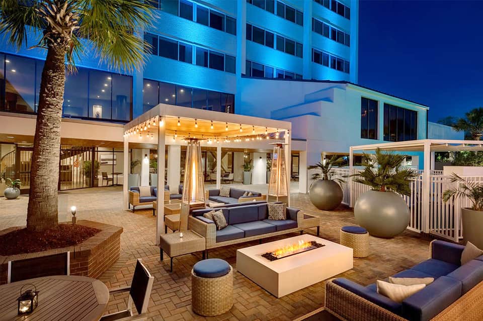 Beachfront resort courtyard at dusk with fire pit, lounge seating, and palm trees