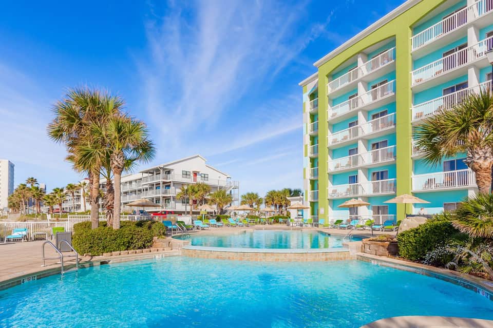 Resort pool with tropical palm trees and colorful multi-story hotel building against blue sky