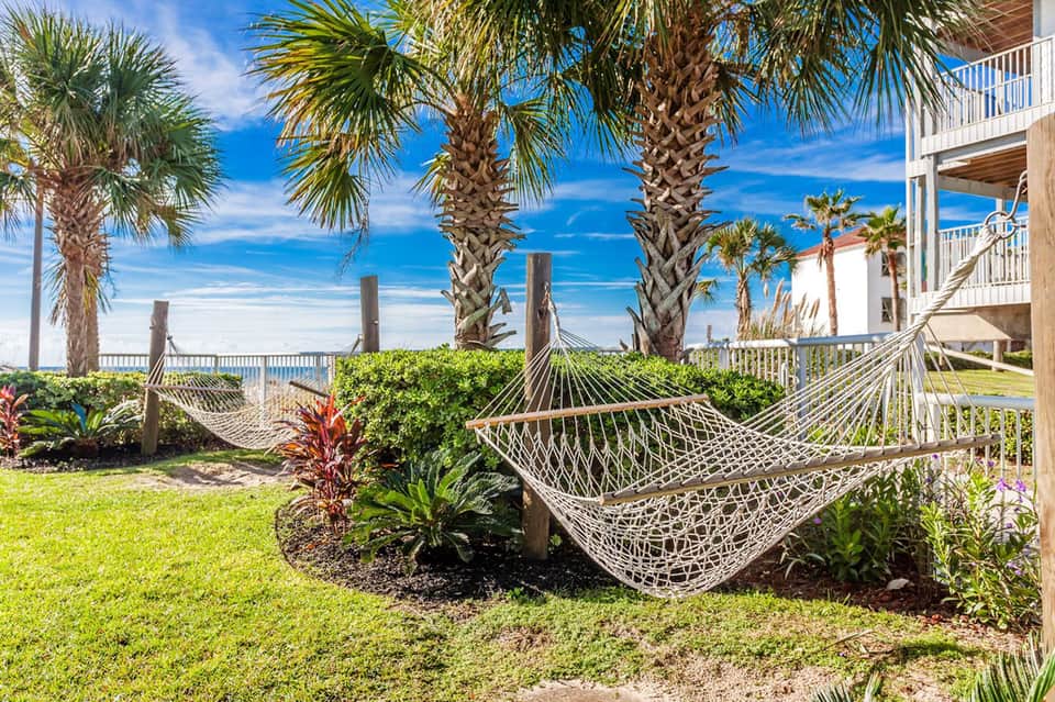 Oceanfront lawn with white hammocks strung between palm trees and beach access
