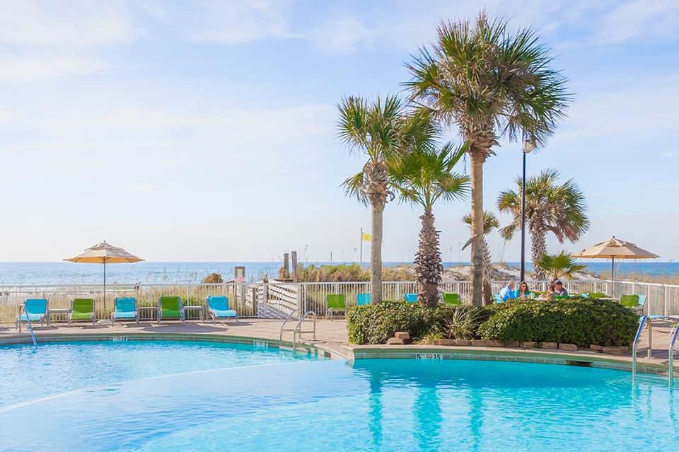 Resort pool with palm trees, umbrellas, and beach access in background