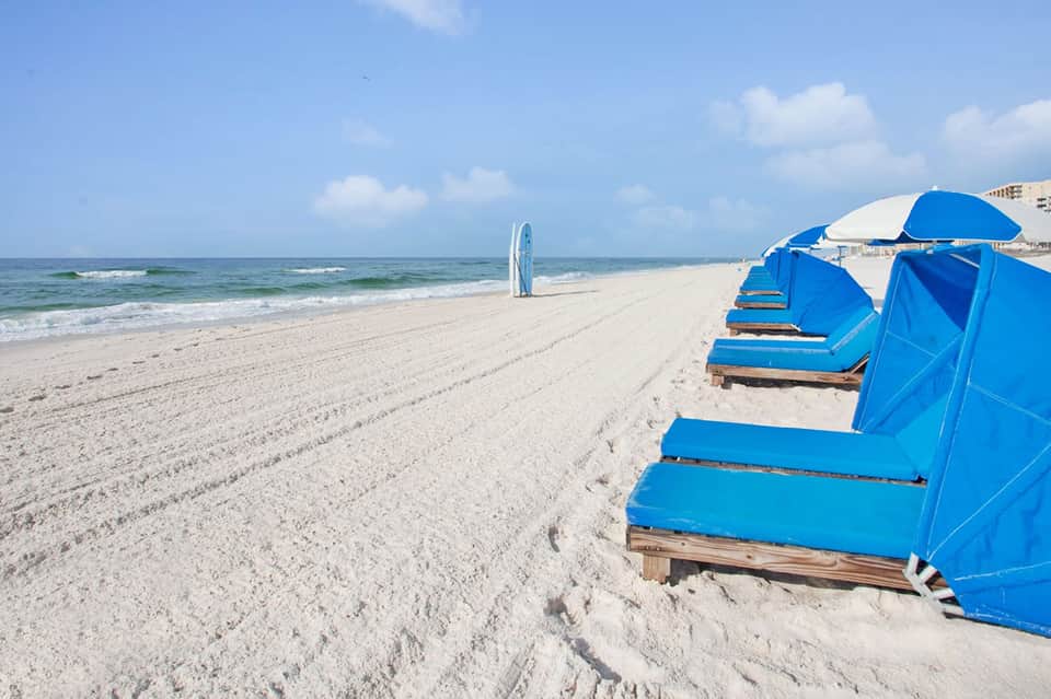Blue beach umbrellas and cabanas lined on sandy beach with surfboard