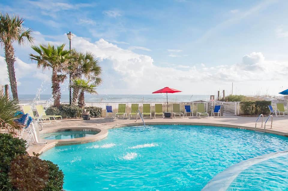 Resort pool with hot tub, red umbrella, and palm trees overlooking the ocean and beach