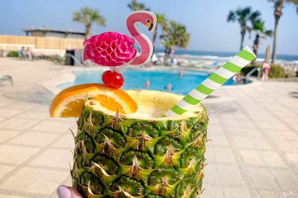 Tropical cocktail in pineapple with flamingo garnish by resort pool and ocean