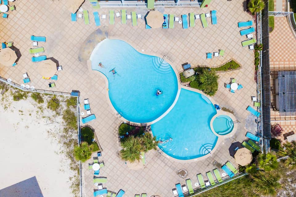 Aerial view of a curved resort pool with lounge chairs and beach access