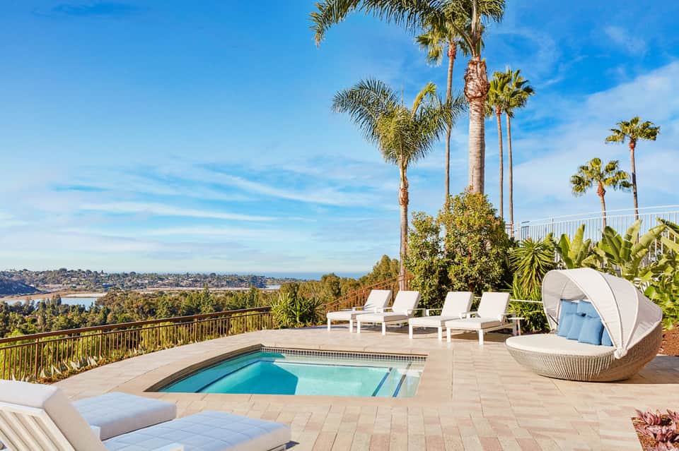 Luxury hilltop pool deck with white lounge chairs, palm trees, and panoramic bay views
