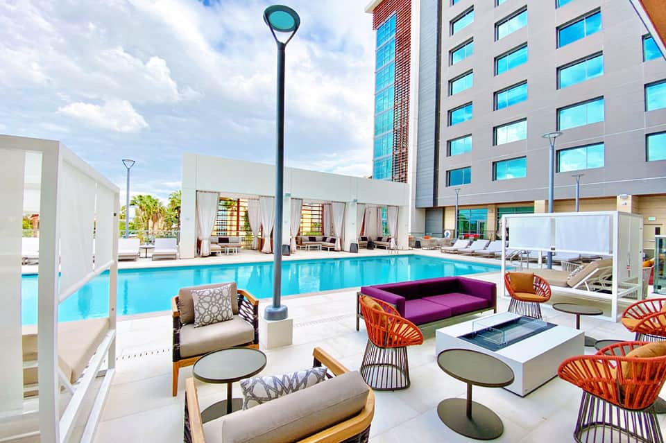 Modern resort pool deck with lounge chairs, colorful seating, and high-rise hotel building