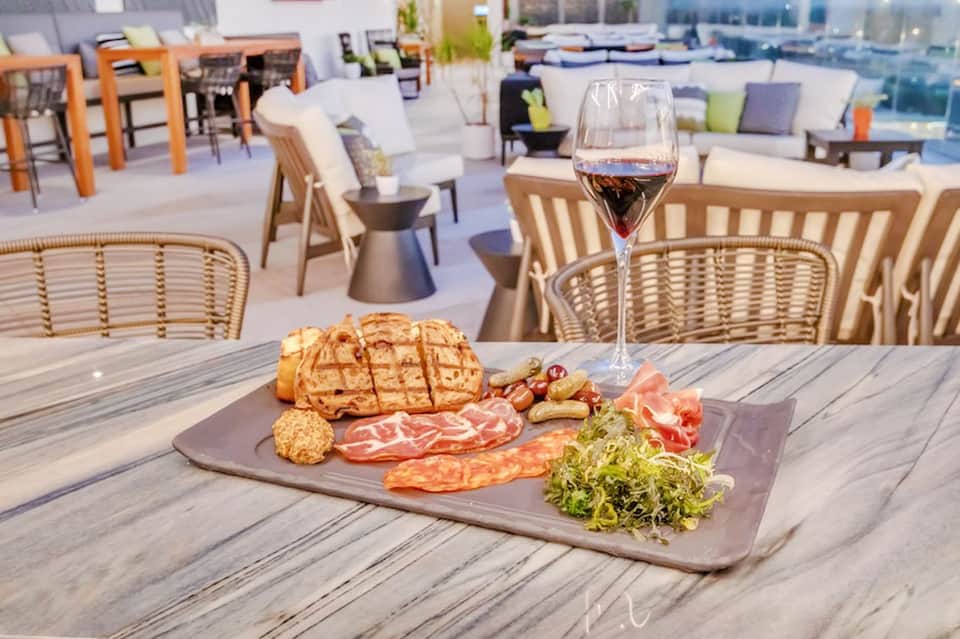 Rooftop terrace with charcuterie board, wine glass, and wicker seating overlooking the city