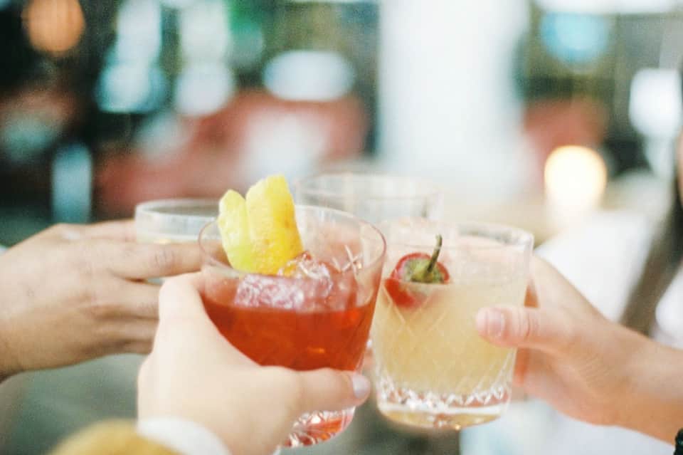 Close-up of two colorful cocktails with citrus garnishes held by people at an event