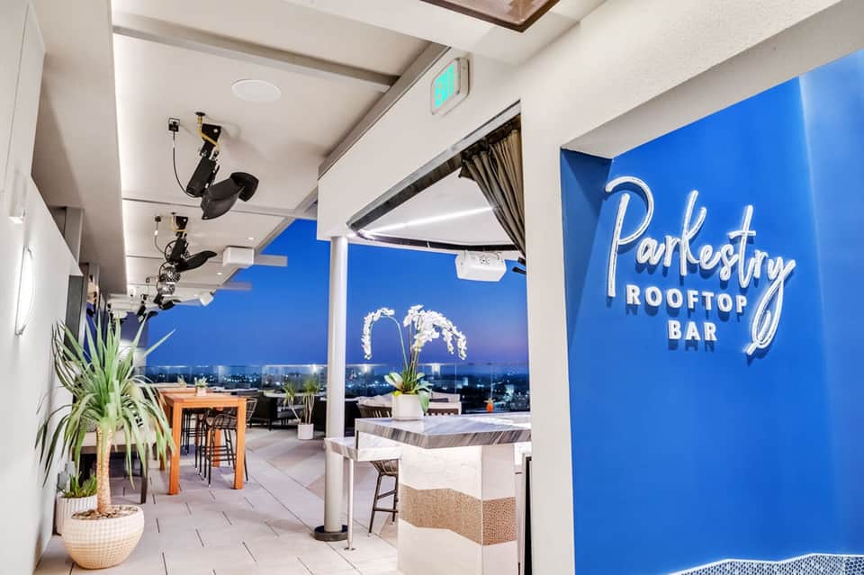 Modern rooftop bar with neon 'Parkestry' sign, city skyline views, and contemporary furnishings