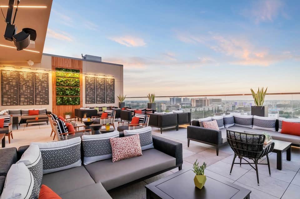 Modern rooftop lounge with contemporary seating, city skyline views, and ambient lighting at dusk