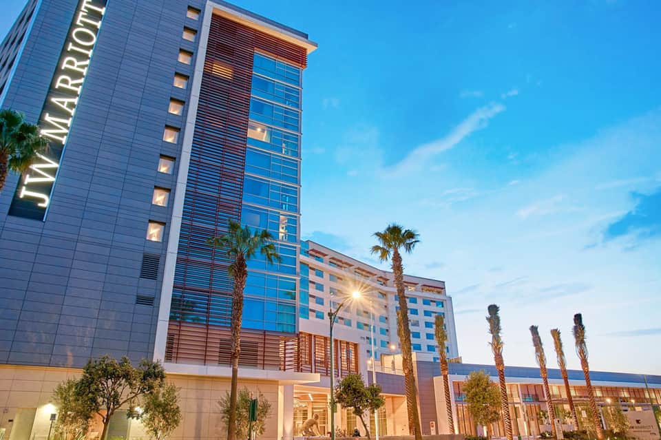 Modern hotel exterior at dusk with glass tower, palm trees, and lit entrance