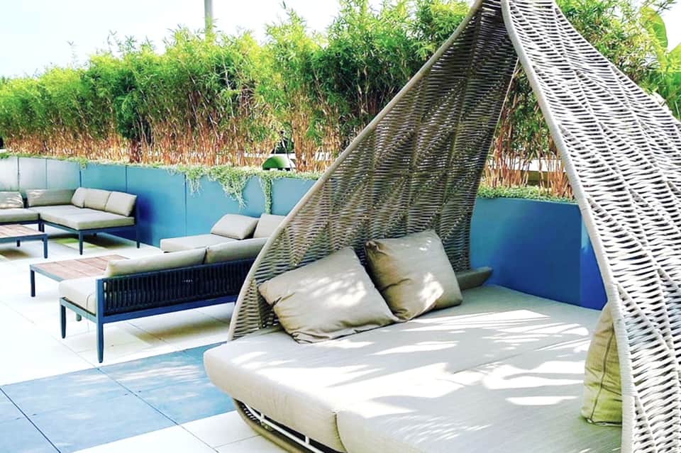 Outdoor lounge area with woven daybed canopy, blue accent wall, and lush green bamboo privacy screening
