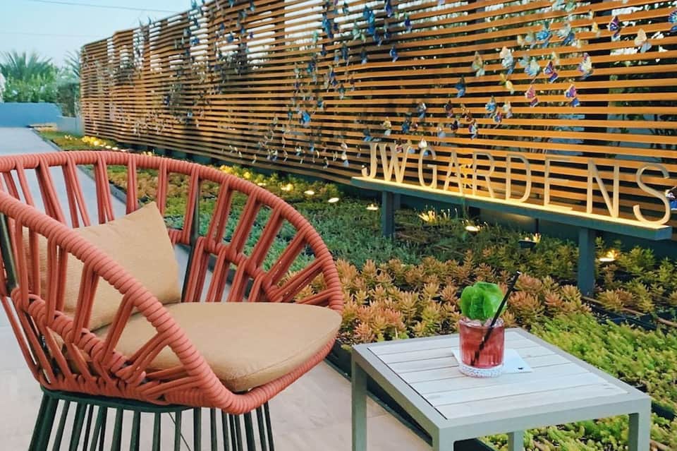Modern pool lounge area with red woven chair, cocktail on table, and decorative wooden fence
