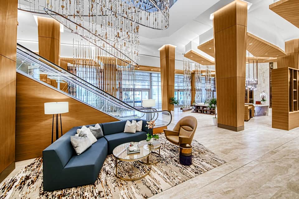 Modern hotel lobby with wooden pillars, chandelier, blue sofa, and escalator to upper floor