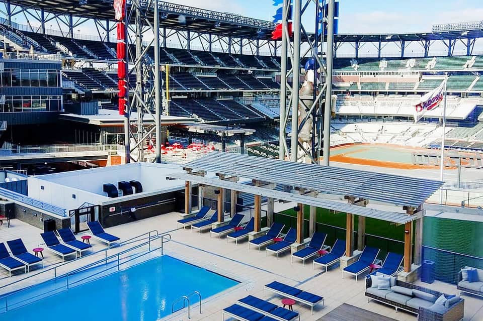 Modern hotel pool deck with blue loungers under metal shade structures overlooking a stadium