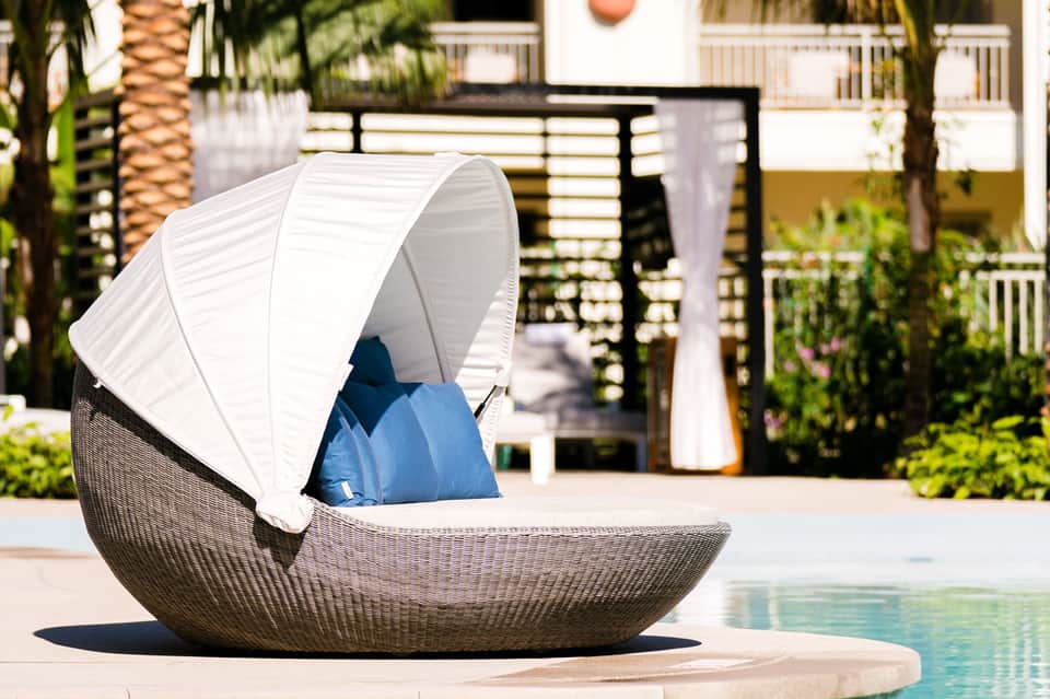 Woven daybed with white canopy and blue cushions beside resort pool and waterfront